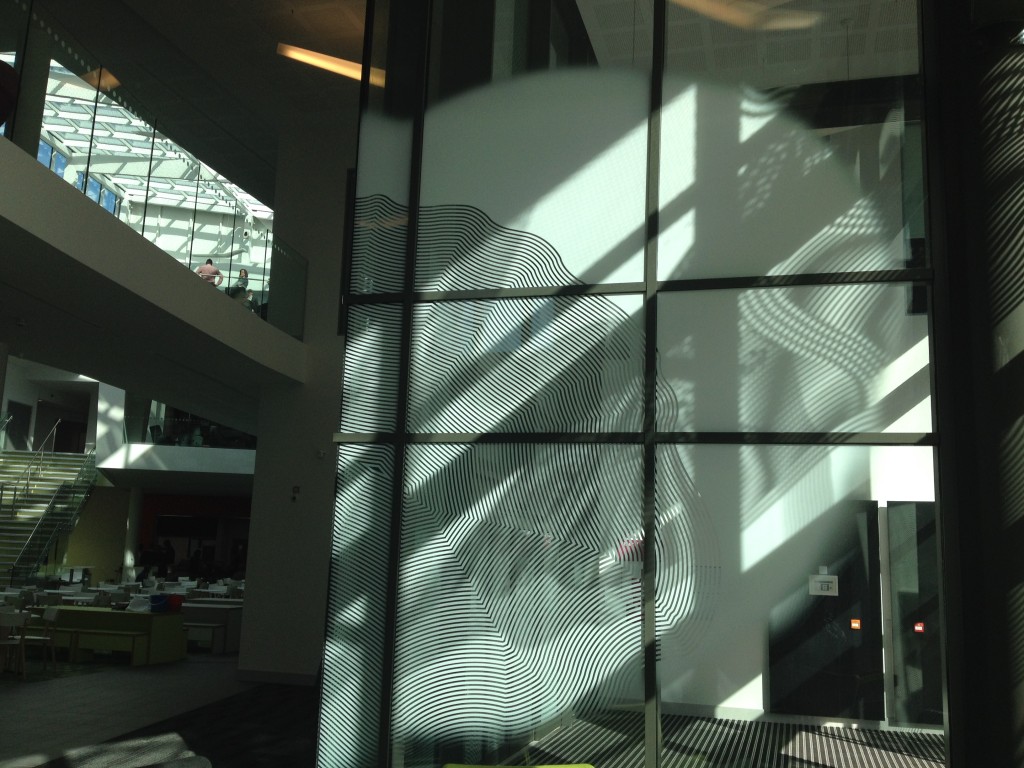 This image shows the manifestation artwork applied to the interior glazed lobby, with the central atrium space just visible on the left. Sheffield Hallam University, Heart of the Campus. Image: Christopher Tipping