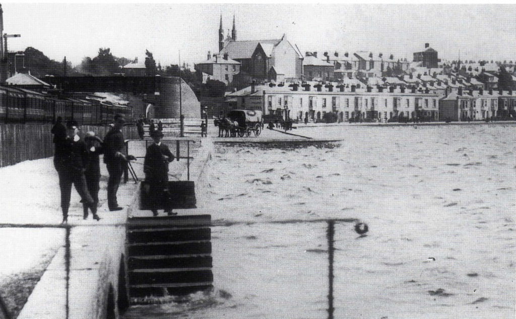 This image of the down side of the track during high tide in 1890 shows just how close the train passed to the shoreline and the waters edge. Weymouth Terrace can be seen in the background. The footbridge is still in use today ! Image: Bert Moody Collection.