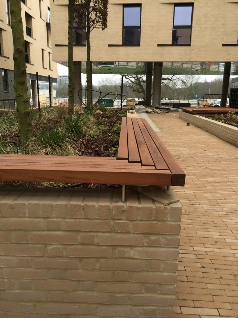 Central Chelmsford for Genesis Housing Association. Detail: slatted  timber seating, part of the embedded public art interpretation carries cnc routed text - image taken during installation on site. Image: Christopher Tipping